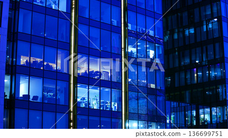 Big glowing windows in modern office building at night, in rows of windows light shines. Fragment of the glass facade of a modern corporate building at night. Modern glass office in city. Big glowing windows in modern office building at night, in rows of windows light shines. Fragment of the glass facade of a modern corporate building at night. Modern glass office in city. 136699751