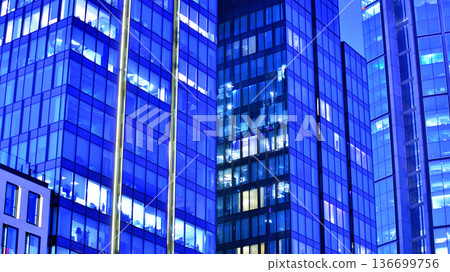 Big glowing windows in modern office building at night, in rows of windows light shines. Fragment of the glass facade of a modern corporate building at night. Modern glass office in city. Big glowing windows in modern office building at night, in rows of windows light shines. Fragment of the glass facade of a modern corporate building at night. Modern glass office in city. 136699756