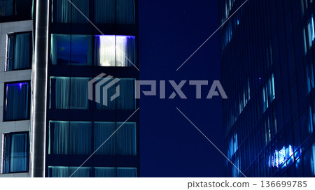 Big glowing windows in modern office building at night, in rows of windows light shines. Fragment of the glass facade of a modern corporate building at night. Modern glass office in city. Big glowing windows in modern office building at night, in rows of windows light shines. Fragment of the glass facade of a modern corporate building at night. Modern glass office in city. 136699785