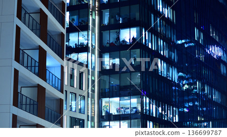 Big glowing windows in modern office building at night, in rows of windows light shines. Fragment of the glass facade of a modern corporate building at night. Modern glass office in city. Big glowing windows in modern office building at night, in rows of windows light shines. Fragment of the glass facade of a modern corporate building at night. Modern glass office in city. 136699787