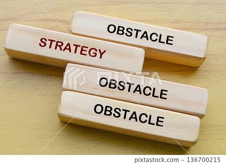 Obstacle and Strategy text on wooden blocks representing overcoming repeated obstacles by transforming barriers into strategic stepping stones for growth and advancement. Obstacle and Strategy text on wooden blocks representing overcoming repeated obstacles by transforming barriers into strategic stepping stones for growth and advancement. 136700215