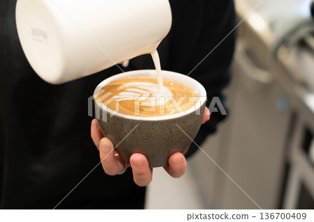 Woman's hands pouring a cafe latte 136700409