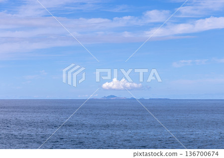 Single cloud over distant Atlantic islands, gentle ocean texture and pale sky near Madeira, Portugal 136700674