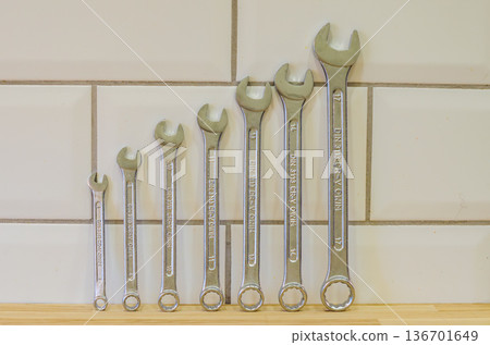 An organized set of chrome vanadium steel wrenches of various sizes, from small to large, arranged on a wooden workbench against a tiled wall.. High quality photo An organized set of chrome vanadium steel wrenches of various sizes, from small to large, arranged on a wooden workbench against a tiled wall.. High quality photo 136701649