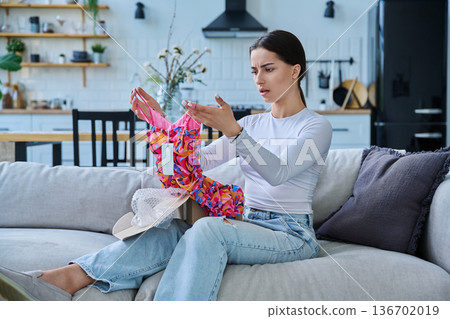Young woman unpacking cardboard box parcel with online order, looking at new clothes 136702019