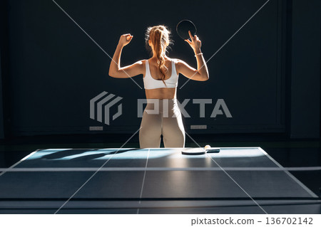 Ready to play, posing. Beautiful young woman is by the tennis table indoors Ready to play, posing. Beautiful young woman is by the tennis table indoors 136702142