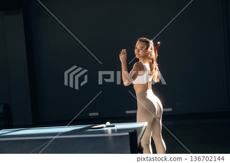 Ready to play, posing. Beautiful young woman is by the tennis table indoors Ready to play, posing. Beautiful young woman is by the tennis table indoors 136702144