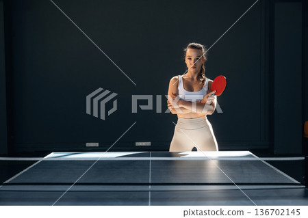 Ready to play, posing. Beautiful young woman is by the tennis table indoors Ready to play, posing. Beautiful young woman is by the tennis table indoors 136702145