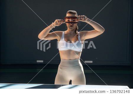 Holding ball between rackets. Beautiful young woman is by the tennis table indoors 136702148