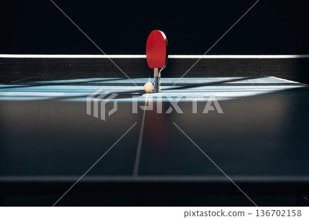 Near to the white net. Racket and ball are on the tennis table indoors 136702158