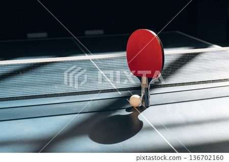 Near to the white net. Racket and ball are on the tennis table indoors Near to the white net. Racket and ball are on the tennis table indoors 136702160