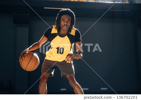Black wall is behind, practicing. Young man is playing basketball indoors 136702201