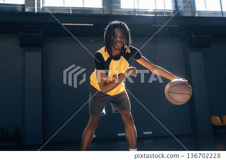 Leading the ball forward. Young black man is playing basketball indoors 136702228