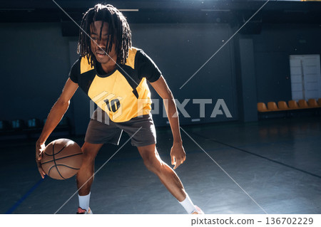 Leading the ball forward. Young black man is playing basketball indoors 136702229