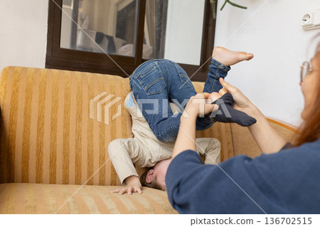 Mother helping playful child getting dressed on sofa Mother helping playful child getting dressed on sofa 136702515