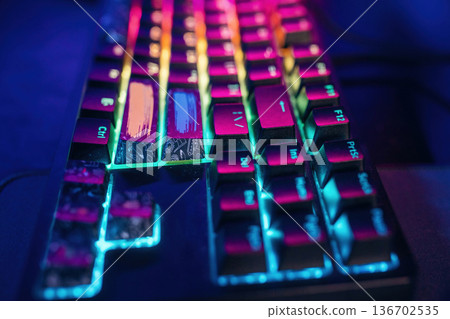 Colorful keyboard. Gaming computer is in the dark room with neon lighting Colorful keyboard. Gaming computer is in the dark room with neon lighting 136702535