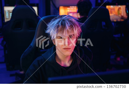 Gamer with white hair is sitting by computer indoors Gamer with white hair is sitting by computer indoors 136702730