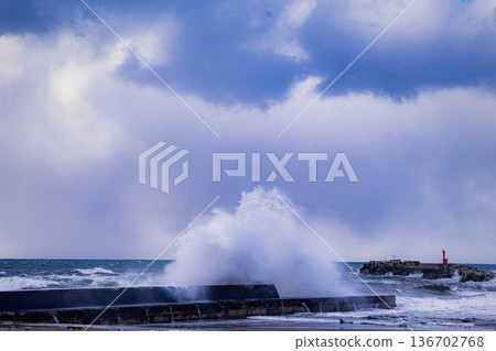 Winter waves of the Sea of Japan crashing against a breakwater: violent spray and a red lighthouse 136702768