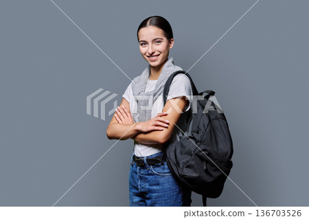 Portrait of confident female teenage student with backpack on gray background Portrait of confident female teenage student with backpack on gray background 136703526