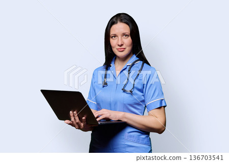 Female nurse holding laptop, looking at camera on white studio background Female nurse holding laptop, looking at camera on white studio background 136703541