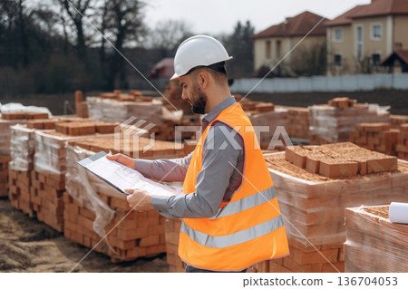 Holding notepad with documents. Construction worker is at job with bricks outdoors 136704053