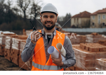 Walkie talkie, radio. Construction worker is at job with bricks outdoors Walkie talkie, radio. Construction worker is at job with bricks outdoors 136704064