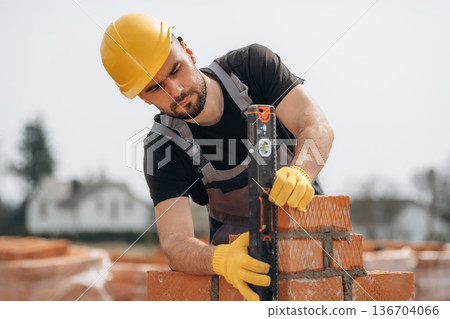 Setting up the right level with tool. Construction worker is at job with bricks outdoors Setting up the right level with tool. Construction worker is at job with bricks outdoors 136704066