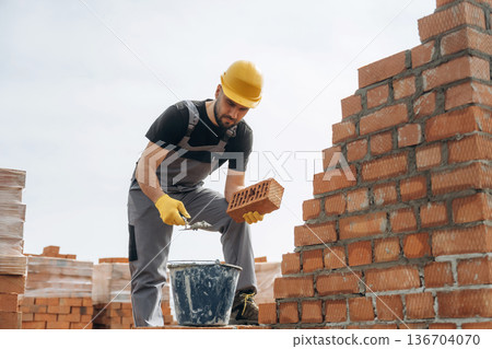 In uniform and hard hat. Construction worker is at job with bricks outdoors 136704070