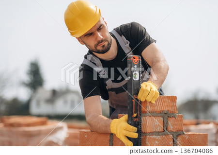 Setting up the right level with tool. Construction worker is at job with bricks outdoors Setting up the right level with tool. Construction worker is at job with bricks outdoors 136704086
