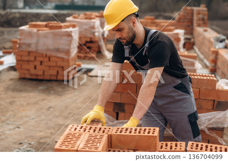 Busy by working with bricks. Construction worker is at job outdoors Busy by working with bricks. Construction worker is at job outdoors 136704099