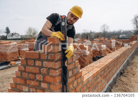 Black colored leveling tool. Construction worker is at job with bricks outdoors Black colored leveling tool. Construction worker is at job with bricks outdoors 136704105