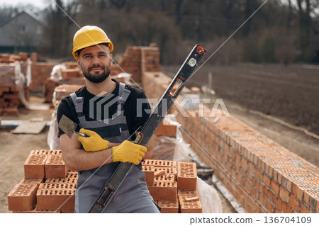 Black colored leveling tool. Construction worker is at job with bricks outdoors Black colored leveling tool. Construction worker is at job with bricks outdoors 136704109