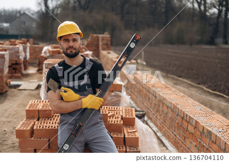 Black colored leveling tool. Construction worker is at job with bricks outdoors Black colored leveling tool. Construction worker is at job with bricks outdoors 136704110