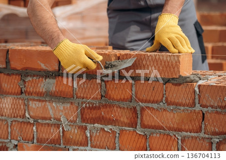 In yellow gloves. Close up view of construction man that is working with bricks 136704113
