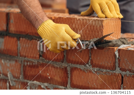 In yellow gloves. Close up view of construction man that is working with bricks In yellow gloves. Close up view of construction man that is working with bricks 136704115