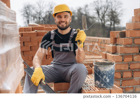 Cheerful positive guy. Construction worker is at job with bricks outdoors 136704116