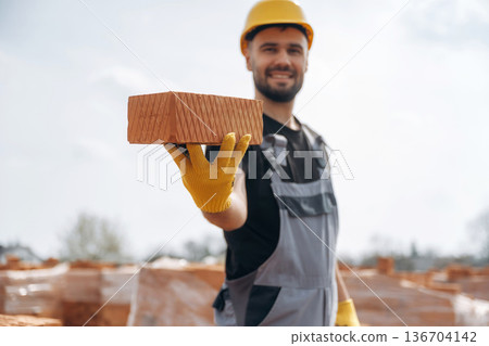 Showing the brick. Construction worker is at job with outdoors Showing the brick. Construction worker is at job with outdoors 136704142
