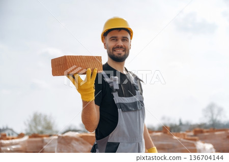 Showing the brick. Construction worker is at job with outdoors Showing the brick. Construction worker is at job with outdoors 136704144