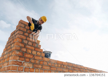 High up, placing bricks. Construction worker is at job outdoors High up, placing bricks. Construction worker is at job outdoors 136704151