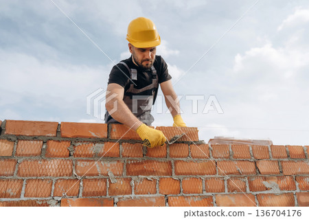 Work in progress. Construction man is at job with bricks outdoors Work in progress. Construction man is at job with bricks outdoors 136704176