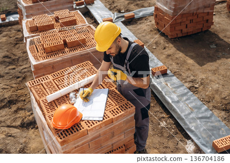 Plan on the paper. Construction worker is at job with bricks outdoors 136704186