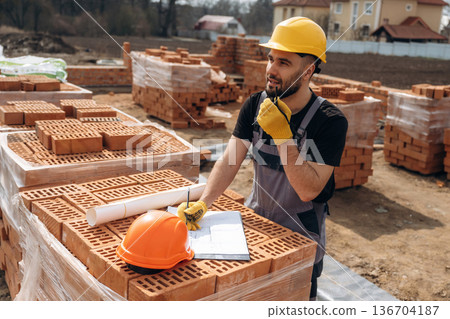 Plan on the paper. Construction worker is at job with bricks outdoors Plan on the paper. Construction worker is at job with bricks outdoors 136704187