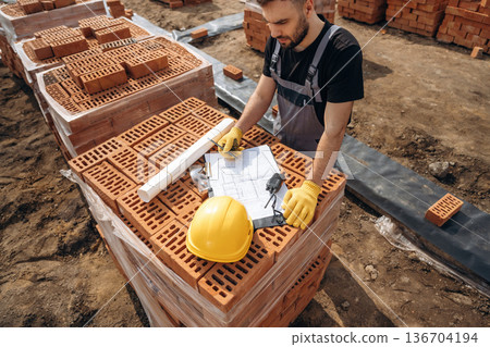 Manager is with project on paper. Construction worker is at job with bricks outdoors Manager is with project on paper. Construction worker is at job with bricks outdoors 136704194