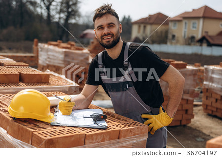 Positive facial expression, standing. Construction worker is at job with bricks outdoors 136704197