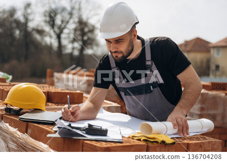 Project plan on the paper. Construction worker is at job with bricks outdoors Project plan on the paper. Construction worker is at job with bricks outdoors 136704208