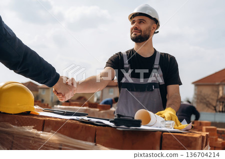 Handshake, making a deal. Cooperation between construction site worker and businessman Handshake, making a deal. Cooperation between construction site worker and businessman 136704214