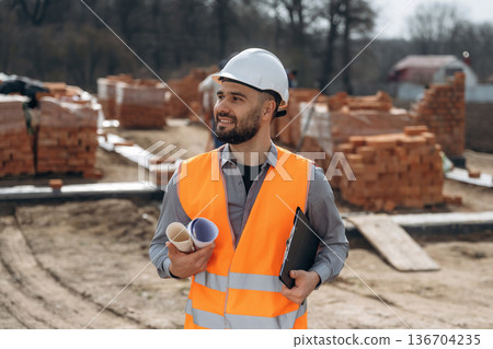 Rolled documents in hand. Construction worker is at job with bricks outdoors 136704235
