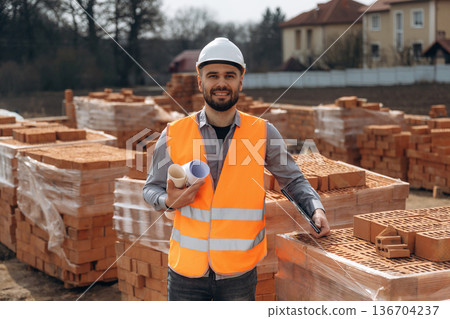 Rolled documents in hand. Construction worker is at job with bricks outdoors 136704237