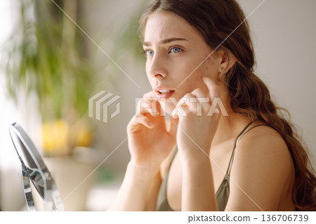 Young woman with problem skin looking into mirror. Concept of acne therapy, scars Young woman with problem skin looking into mirror. Concept of acne therapy, scars 136706739