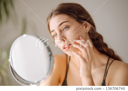 Young woman with problem skin looking into mirror. Concept of acne therapy, scars Young woman with problem skin looking into mirror. Concept of acne therapy, scars 136706740
